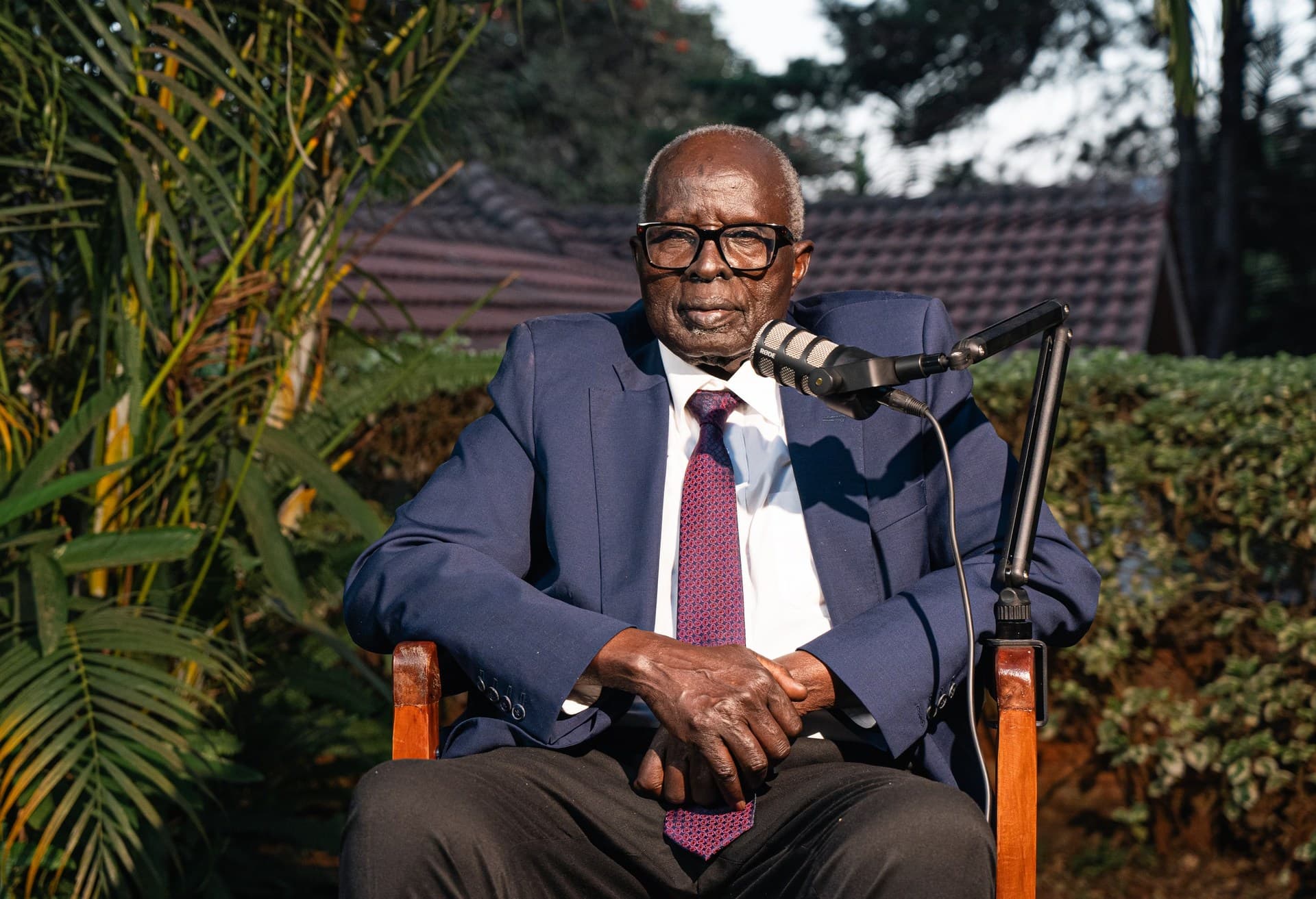 Dr. Aldo Ajou Deng-Akuey seated in the garden, hands folded, listening.