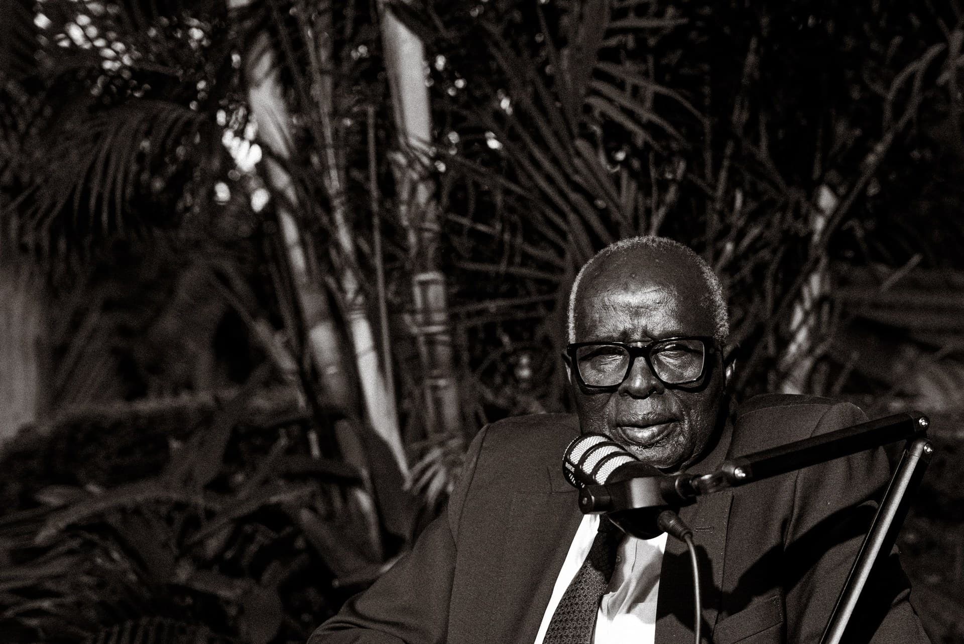 A black-and-white close portrait of Dr. Aldo Ajou Deng-Akuey speaking into the microphone.